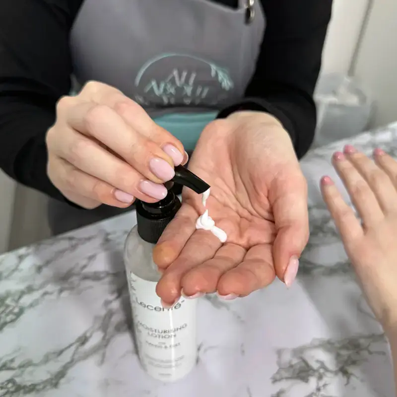 A person dispenses white moisturising lotion onto their palm from a pump bottle, with another hand resting nearby on a marble surface.