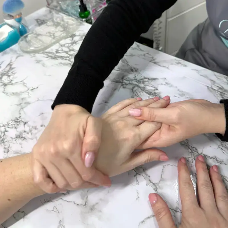 A person receives a hand massage at a marble-topped table, with both hands being gently held and massaged by another person with neatly manicured nails.