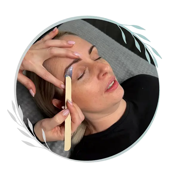 A woman lies with her eyes closed whilst a person applies wax to her eyebrow using a wooden spatula, preparing for an eyebrow waxing treatment at a Hands & Feet Treatments Ipswich salon.